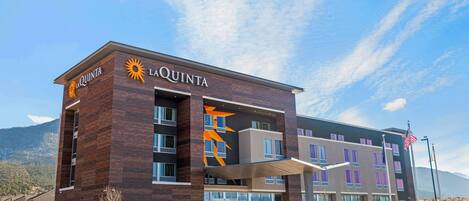A La Quinta hotel with a modern design, featuring a prominent sun logo, multiple windows, and a parking sign indicating overflow parking.