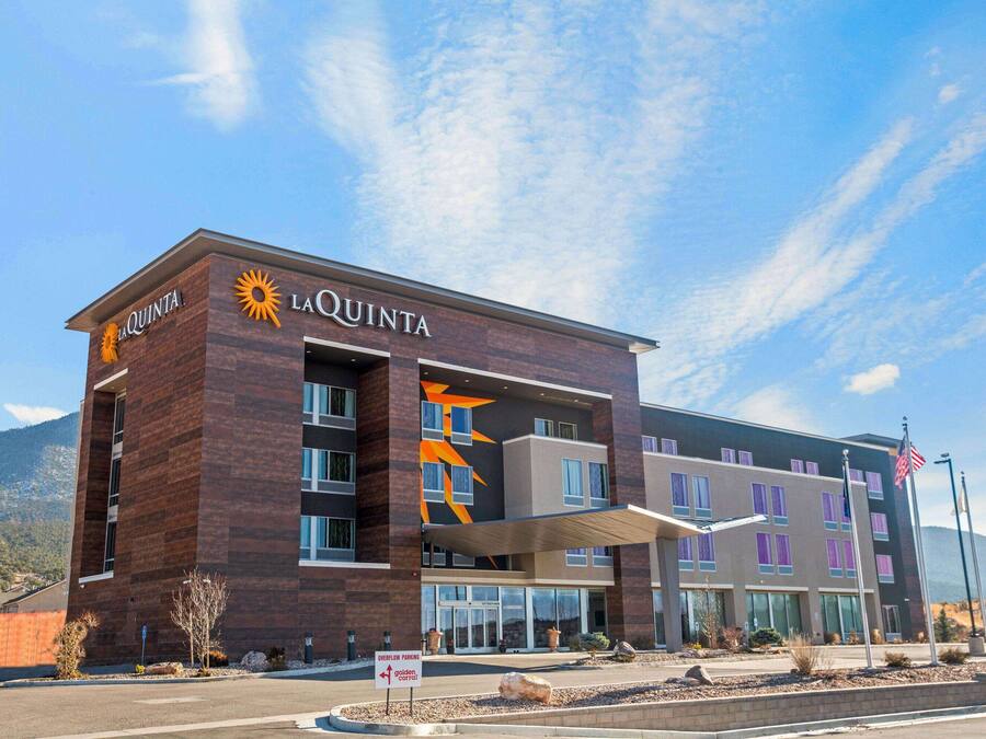 A La Quinta hotel with a modern design, featuring a prominent sun logo, multiple windows, and a parking sign indicating overflow parking.
