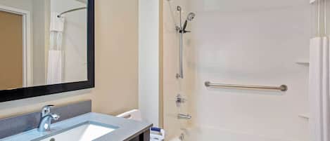 A bathroom with a sink, mirror, shower, and towel rack.