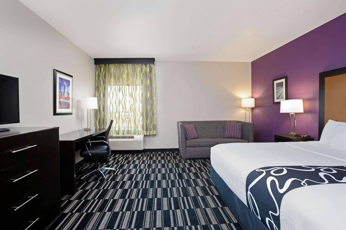 Una habitación de hotel con cama, escritorio, silla y ventana con cortinas.