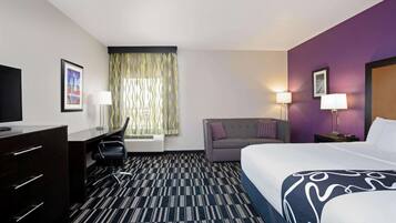 A hotel room with a bed, desk, chair, and a window with curtains.