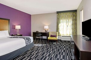 A hotel room with a bed, desk, chair, and TV.