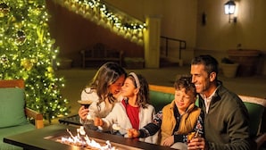 A family sitting by a fire pit with a Christmas tree in the background. - Hotel Viata (Austin)