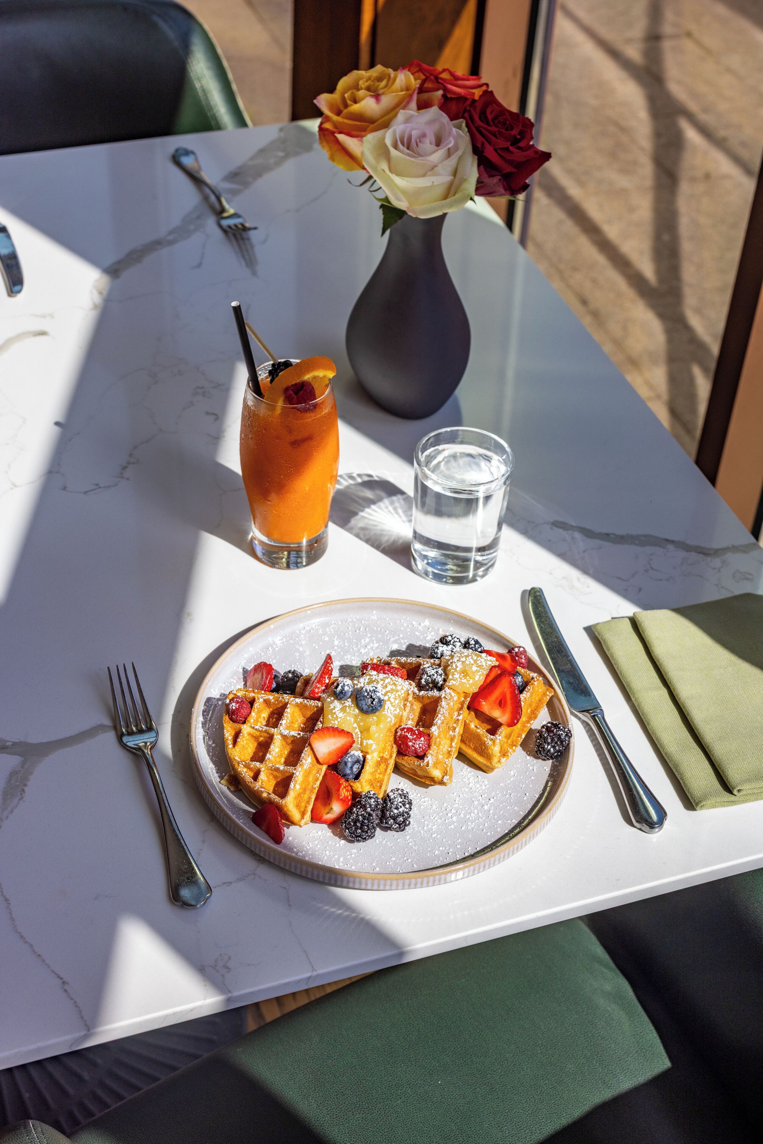 Desayuno con waffles, bayas y una bebida sobre una mesa de mármol.