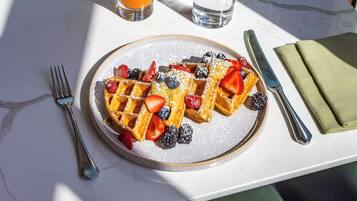 Desayuno con waffles, bayas y una bebida sobre una mesa de mármol.