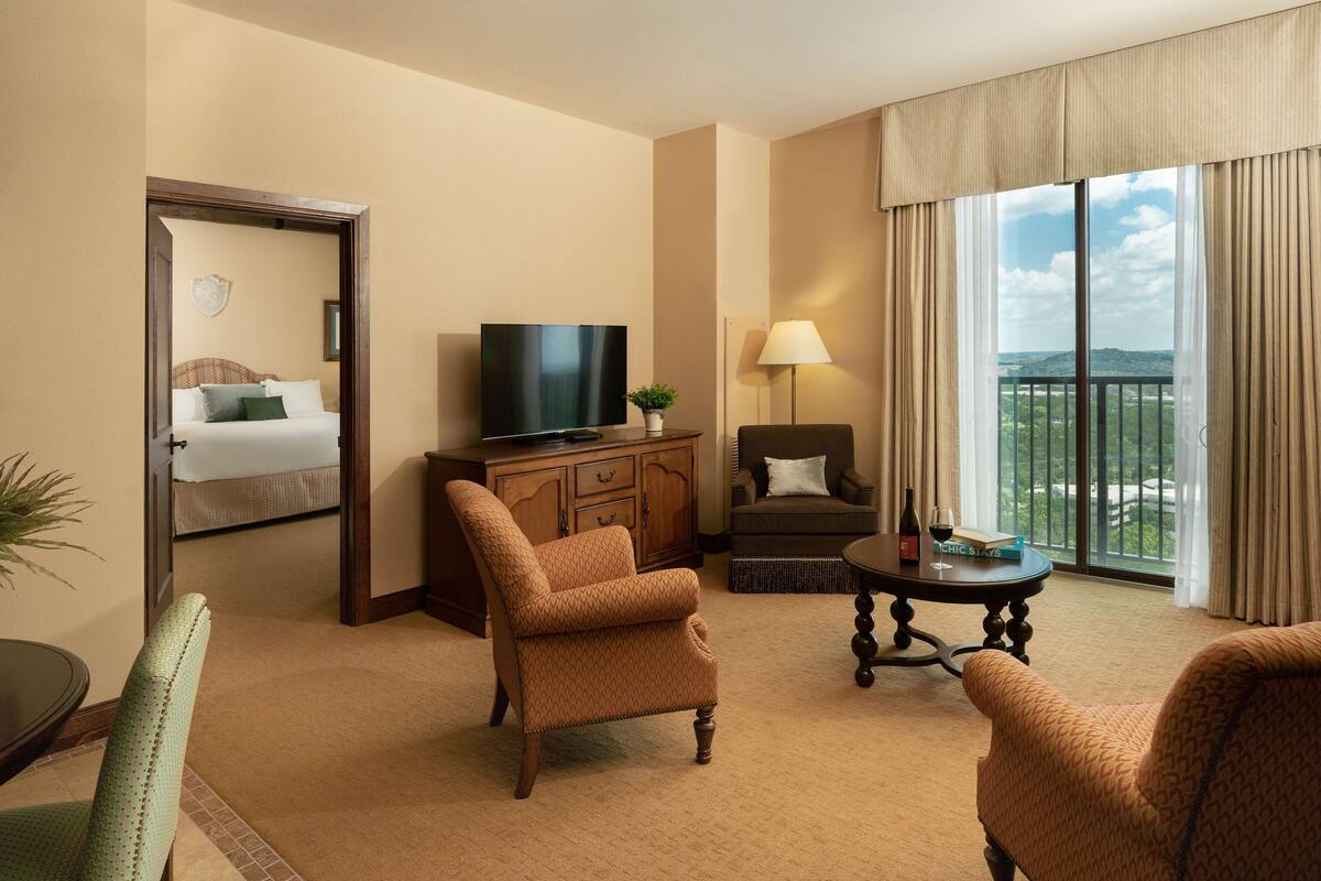 A hotel room with a bed, a TV, a sofa, a chair, a table, and a view of the outdoors.