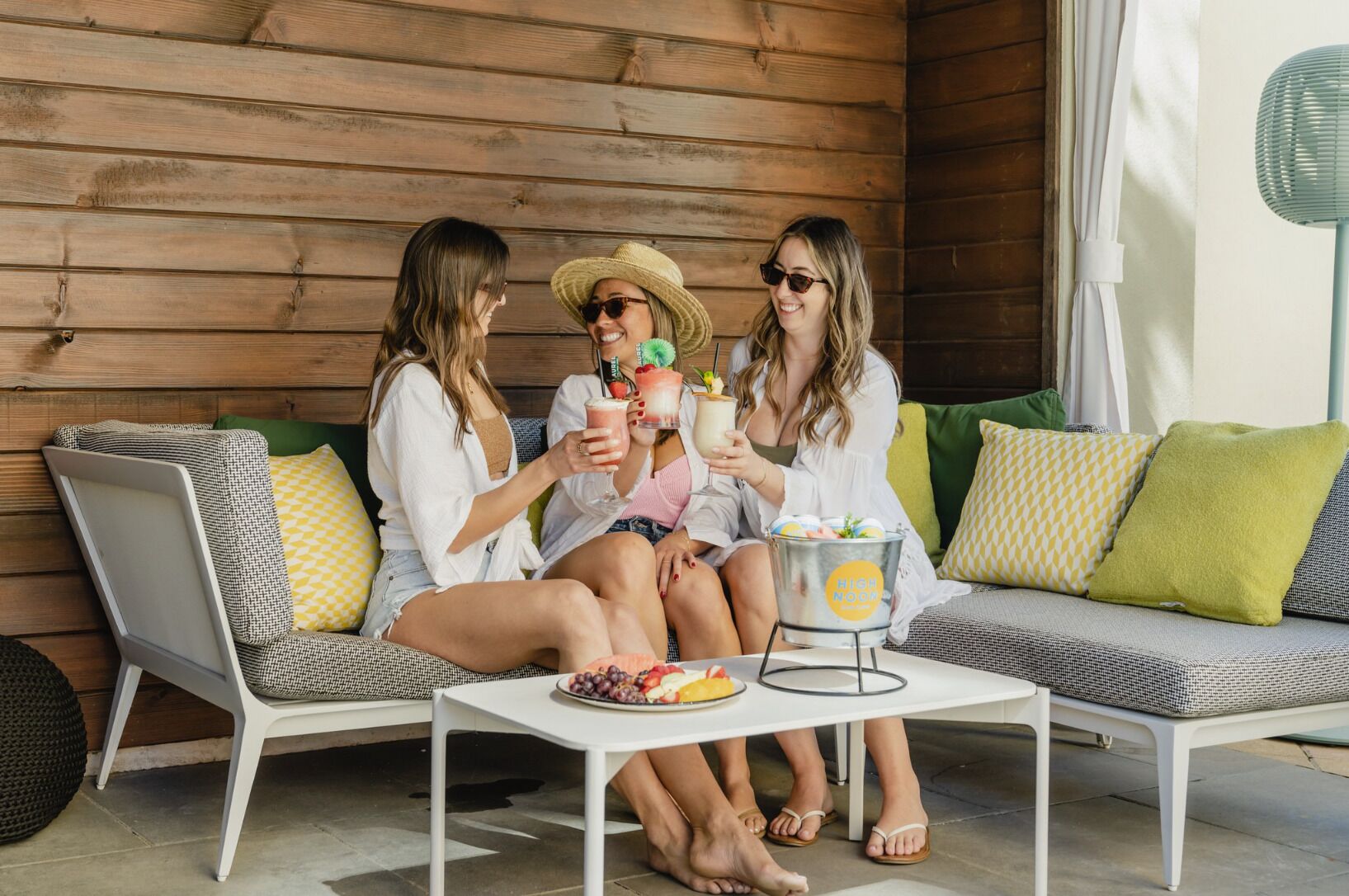 Three people sitting on a white lounge chair and sofa, holding drinks and a bucket of ice cream.