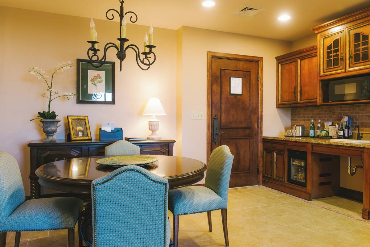 A dining area with a round table, blue upholstered chairs, a chandelier, a framed picture, and a potted orchid.