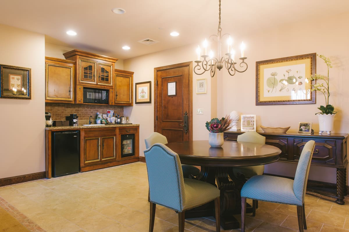 A dining area with a round table, four chairs, wooden cabinets, a chandelier, and framed artwork on the walls.