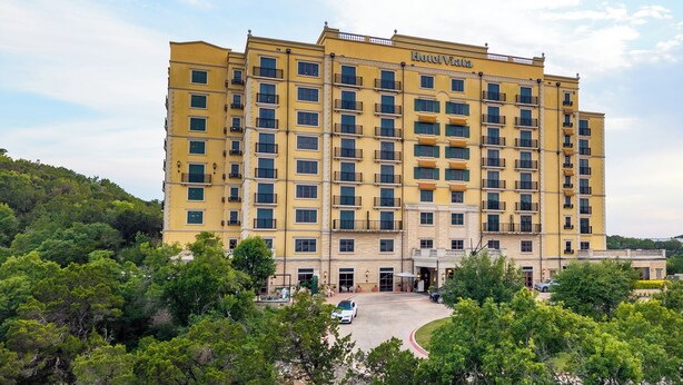 A multi-story hotel with a yellow facade, balconies, and a parking area in front. - Hotel Viata (Austin)