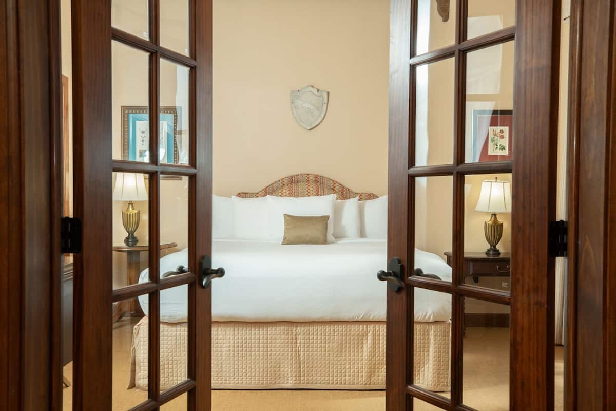A hotel room with a large bed, a headboard with a decorative pattern, two bedside tables with lamps, and a wall-mounted shield-shaped decoration.