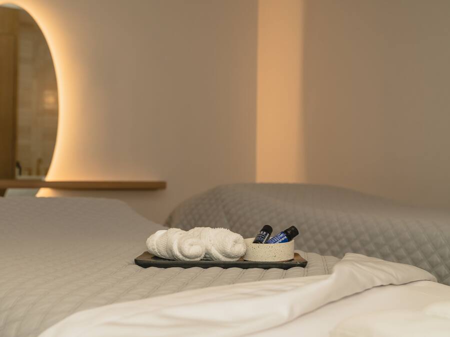 Una cama bien hecha con una bandeja de artículos de aseo, que incluye una toalla y botellas, en una habitación de hotel con un espejo grande y una mesita de noche de madera.