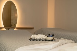 Un lit bien fait, avec un plateau contenant des articles de toilette, notamment une serviette et des flacons, dans une chambre d’hôtel dotée d’un grand miroir et d’une table de chevet en bois.