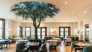 A spacious dining area with wooden flooring, green upholstered chairs, and a large tree sculpture in the center. - Hotel Viata (Austin)