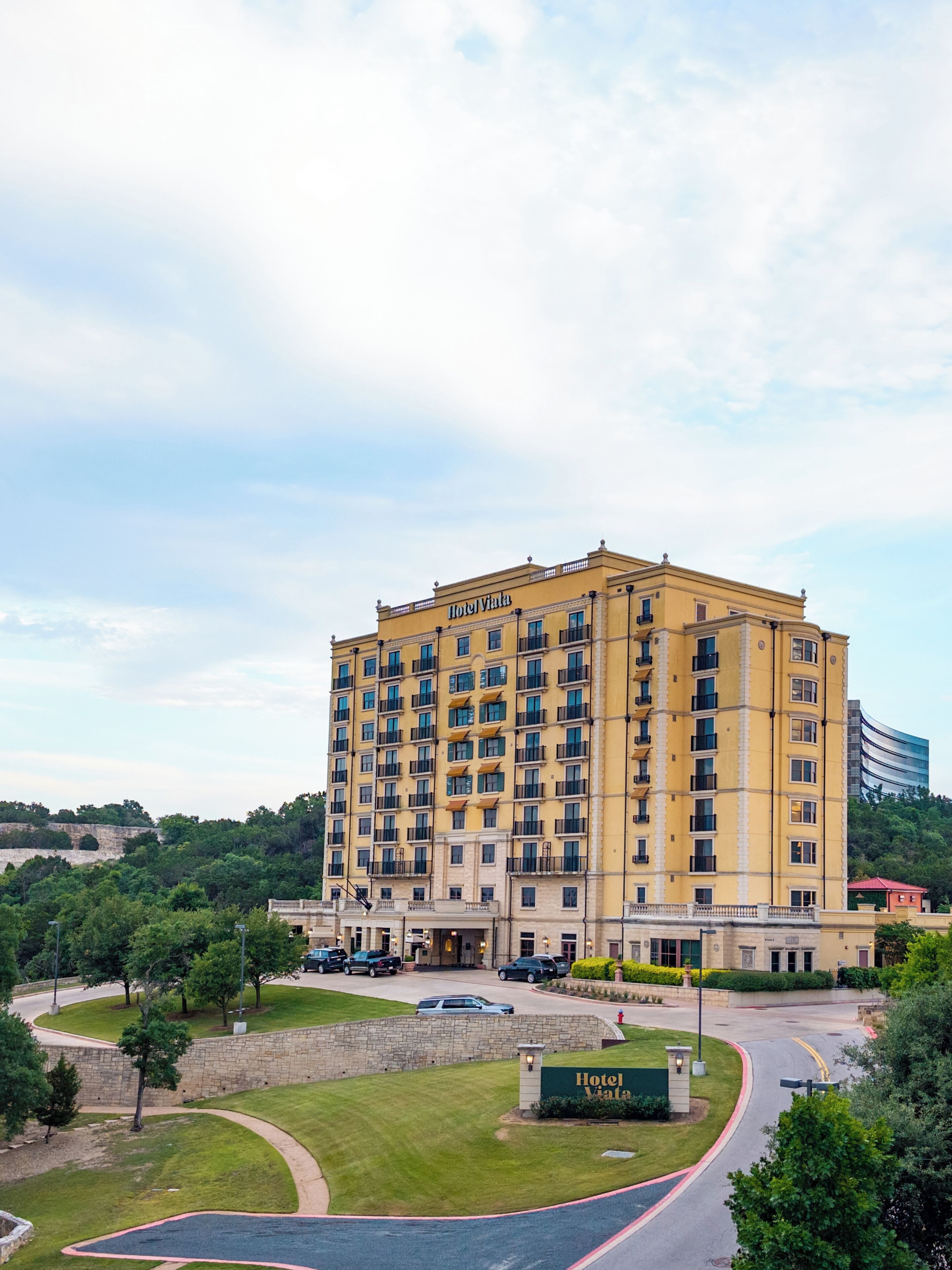 A multi-story hotel with a yellow facade, multiple balconies, and a well-maintained lawn area in front.
