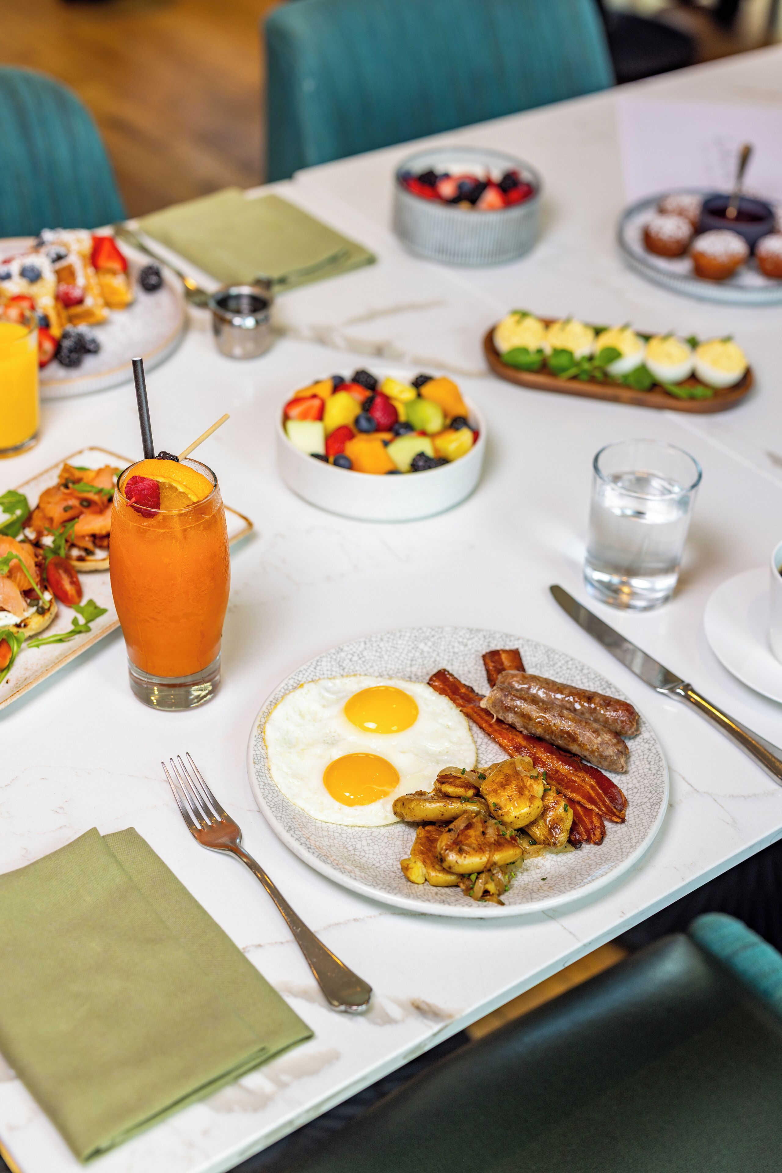 A breakfast table with various dishes including eggs, bacon, and a fruit bowl.