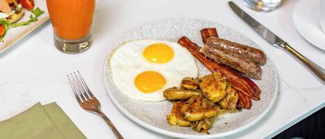 Una mesa de desayuno con diferentes platos, incluyendo huevos, tocino y un bol de fruta.