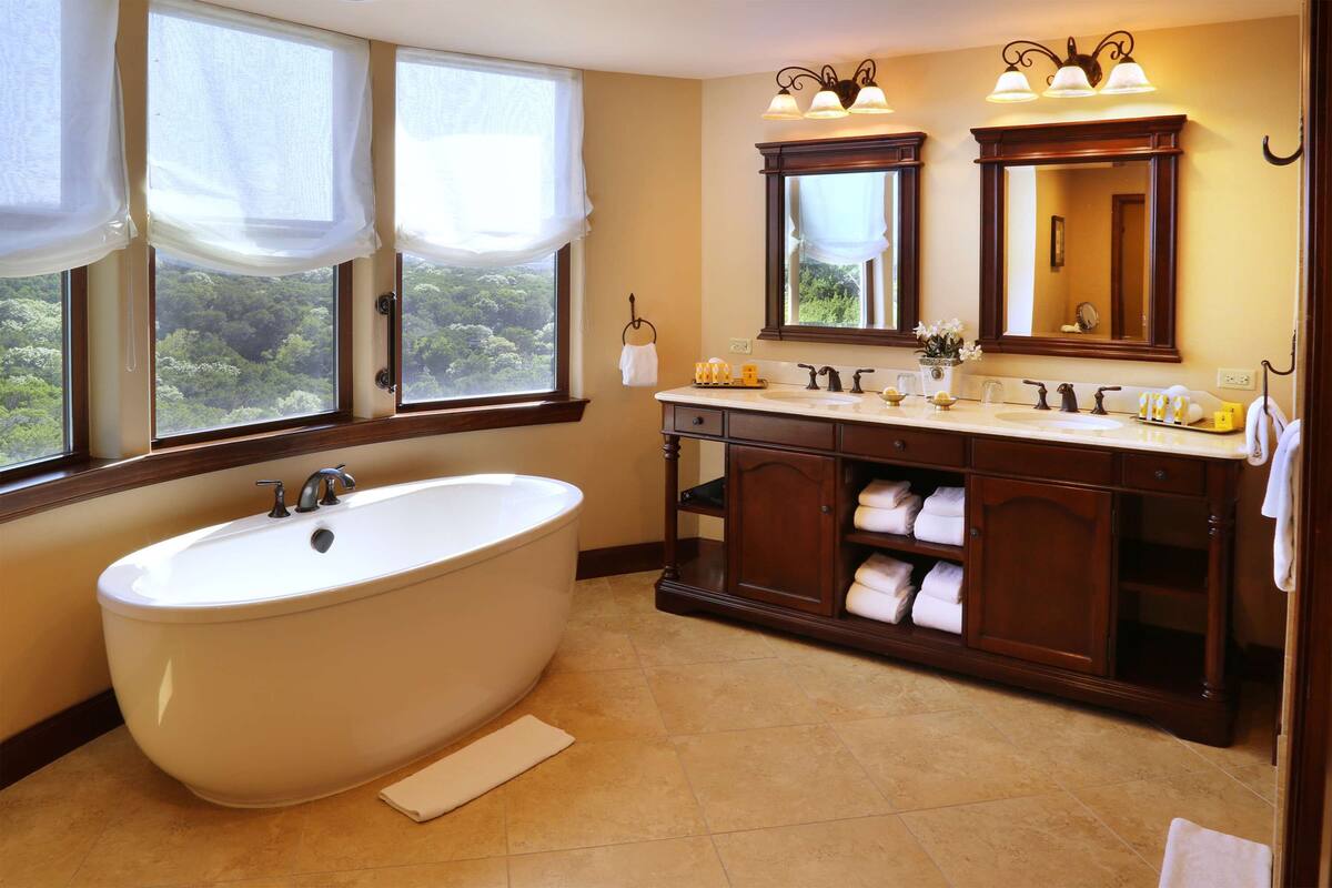 A bathroom with a freestanding bathtub, a double vanity with a mirror above, and a window with curtains.