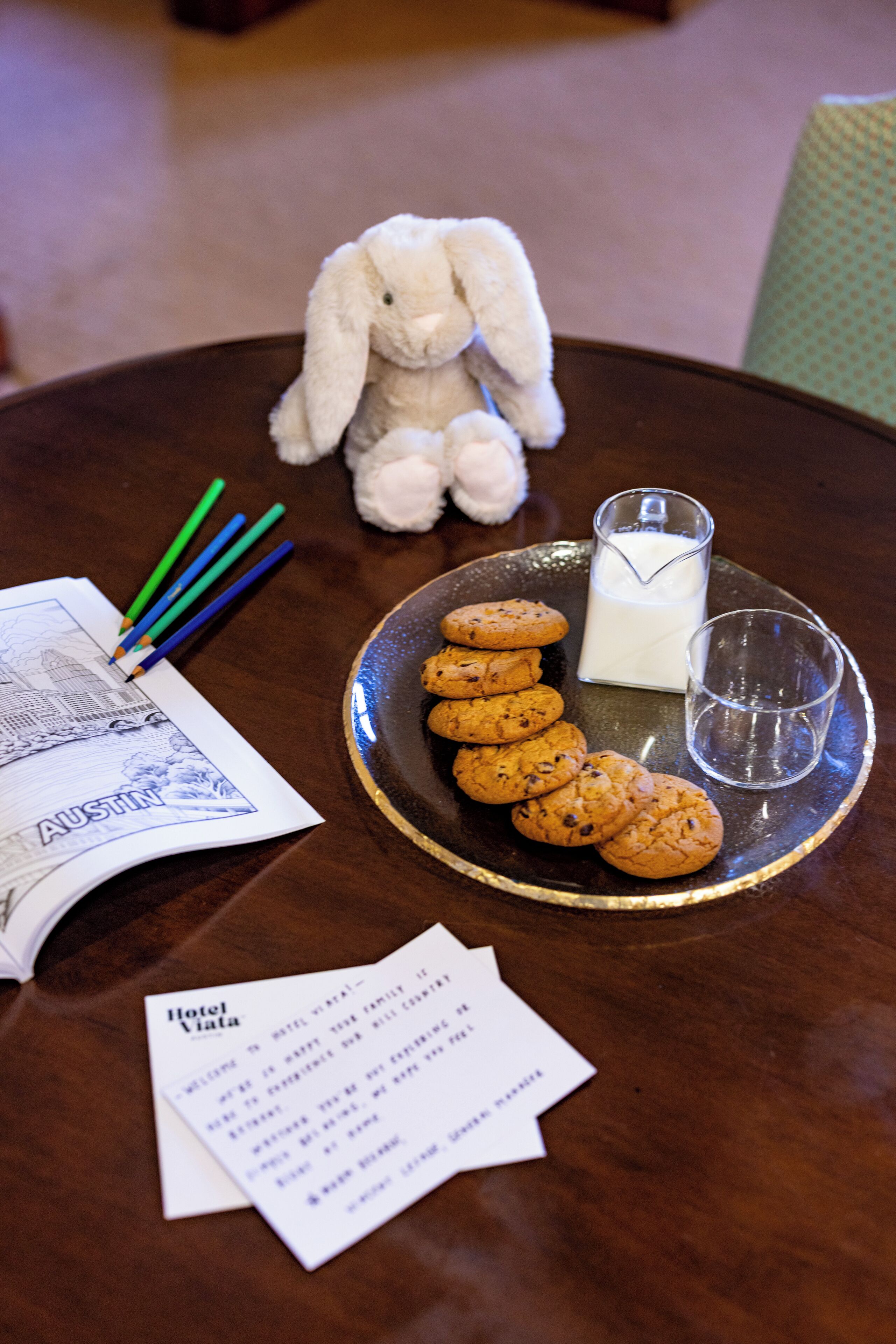 A table with a plate of cookies, a glass of milk, a stuffed toy, and some stationery items.