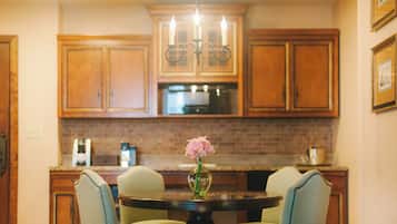 Una cocina con armarios de madera, una araña, una mesa redonda con sillas y un jarrón con flores.