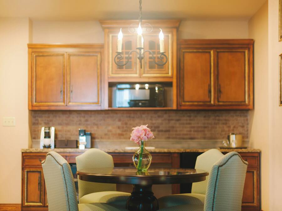 Una cocina con armarios de madera, una araña, una mesa redonda con sillas y un jarrón con flores.