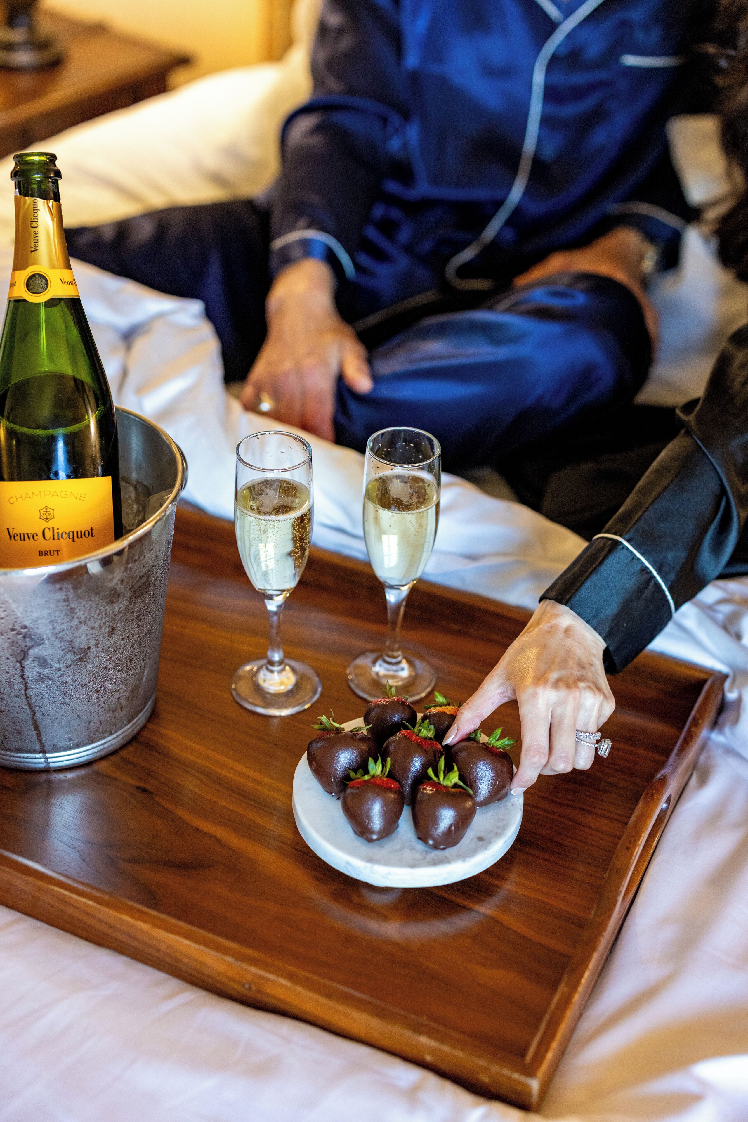 A bottle of Veuve Clicquot champagne, two glasses of champagne, and a plate of chocolate-covered strawberries on a tray.