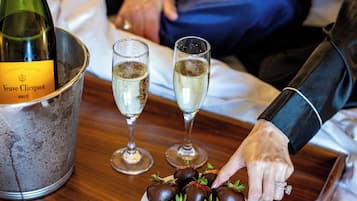 A bottle of Veuve Clicquot champagne, two glasses of champagne, and a plate of chocolate-covered strawberries on a tray.