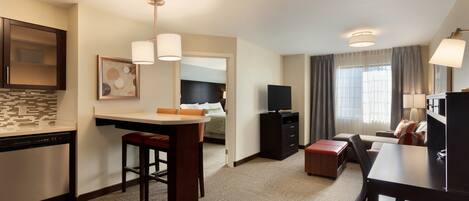 A hotel room with a kitchenette, a dining area, a TV, and a bed.