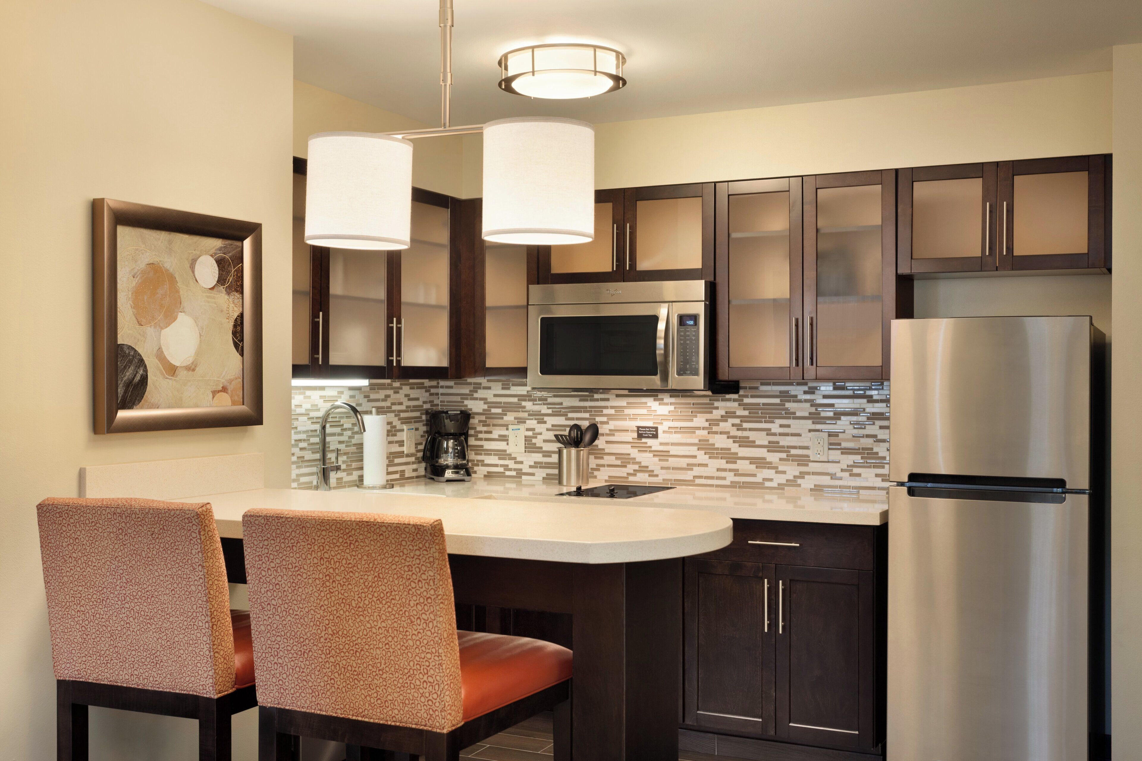 A modern kitchen with dark cabinets, stainless steel appliances, a white countertop, and two pendant lights.