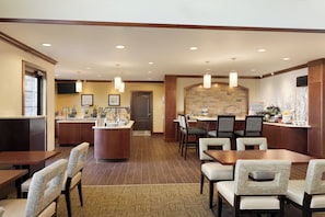 A hotel dining area with a central island, seating arrangements, and a kitchen in the background. - Staybridge Suites Midland by IHG (Midland)
