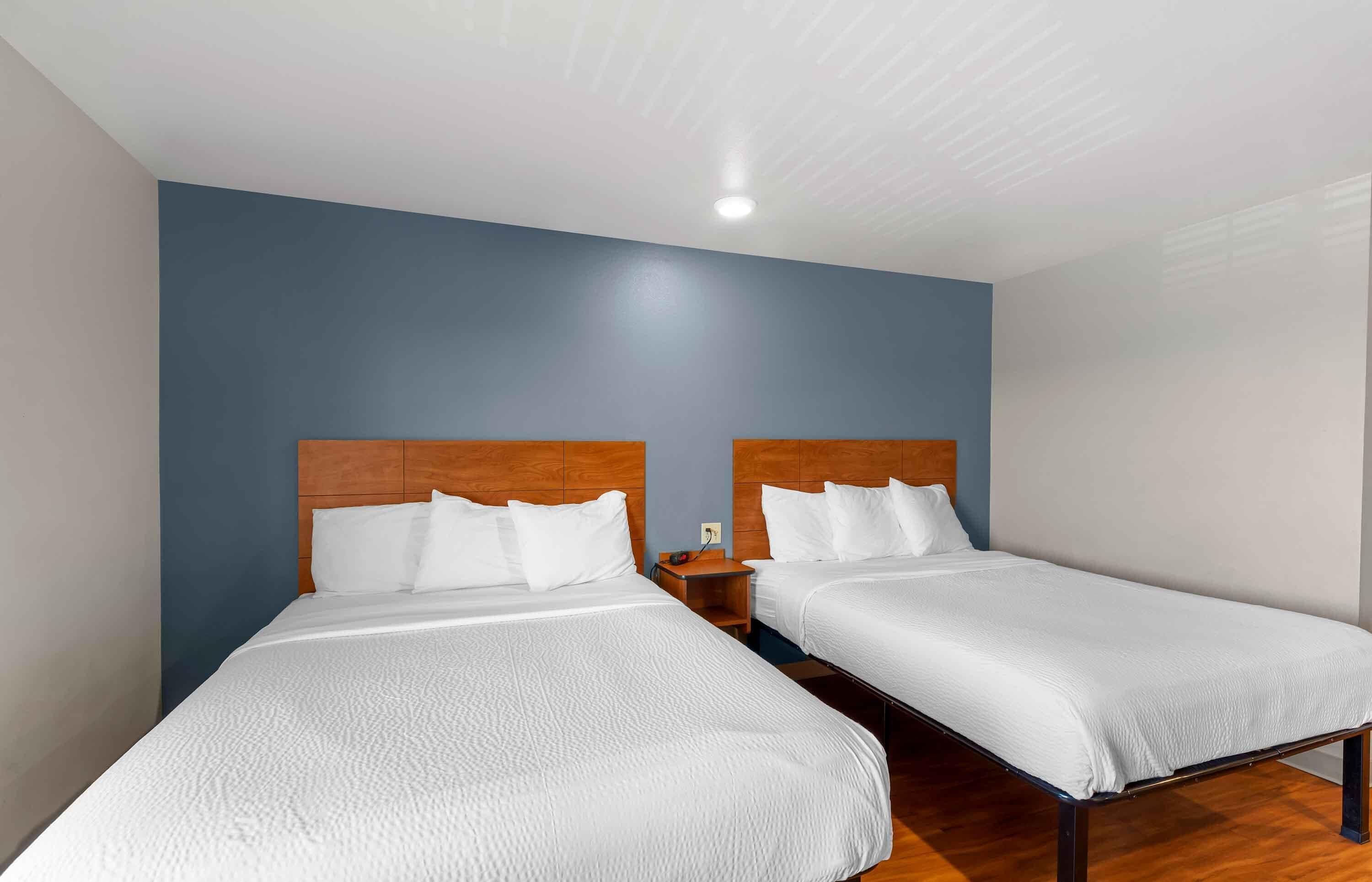 A hotel room with two single beds, wooden headboards, white bedding, and a wooden floor.