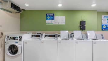 Un lavadero con varias lavadoras y secadoras, un terminal de pago en la pared y carteles informativos.