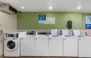 A laundry facility with multiple washing machines and dryers, a wall-mounted payment terminal, and informational posters. - Extended Stay America Suites - Denver - Airport (Aurora)