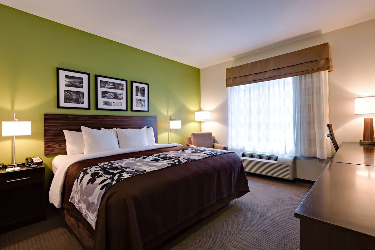 Une chambre d’hôtel comprenant un lit, des tables de chevet, un bureau, une chaise, une fenêtre avec des rideaux et des œuvres d’art accrochées au mur.