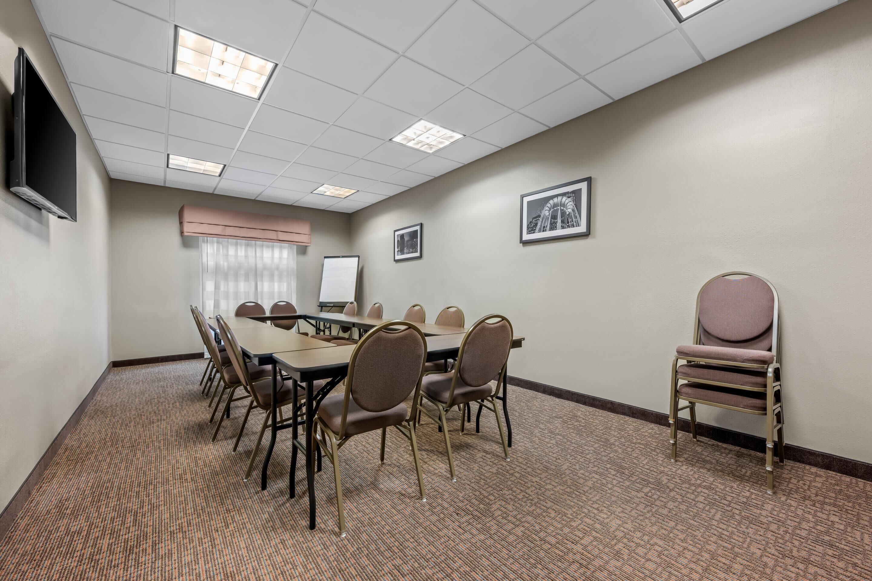 A conference room with a long table, chairs, a projector screen, and framed pictures on the wall.