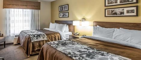 A hotel room with two beds, a desk, a chair, and a window with curtains.