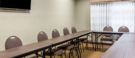 Un salón de conferencias con una mesa larga y sillas, un televisor de pantalla plana en la pared y una ventana con cortinas.
