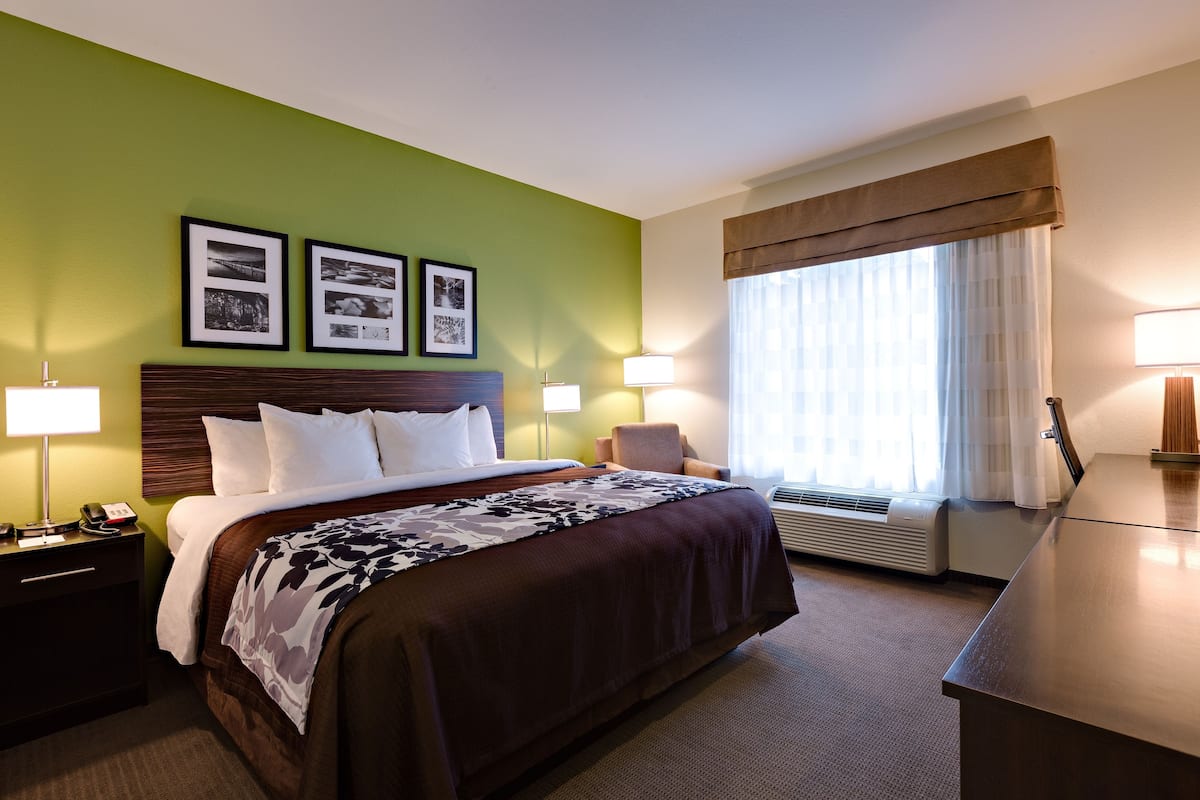 Une chambre d’hôtel avec un grand lit, un bureau, une chaise et une fenêtre avec des rideaux.