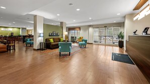 Un hall d’entrée spacieux doté d’un plancher en bois, d’un comptoir de réception, d’un espace salon avec des canapés et des fauteuils, et d’une grande fenêtre offrant une vue sur la rue.