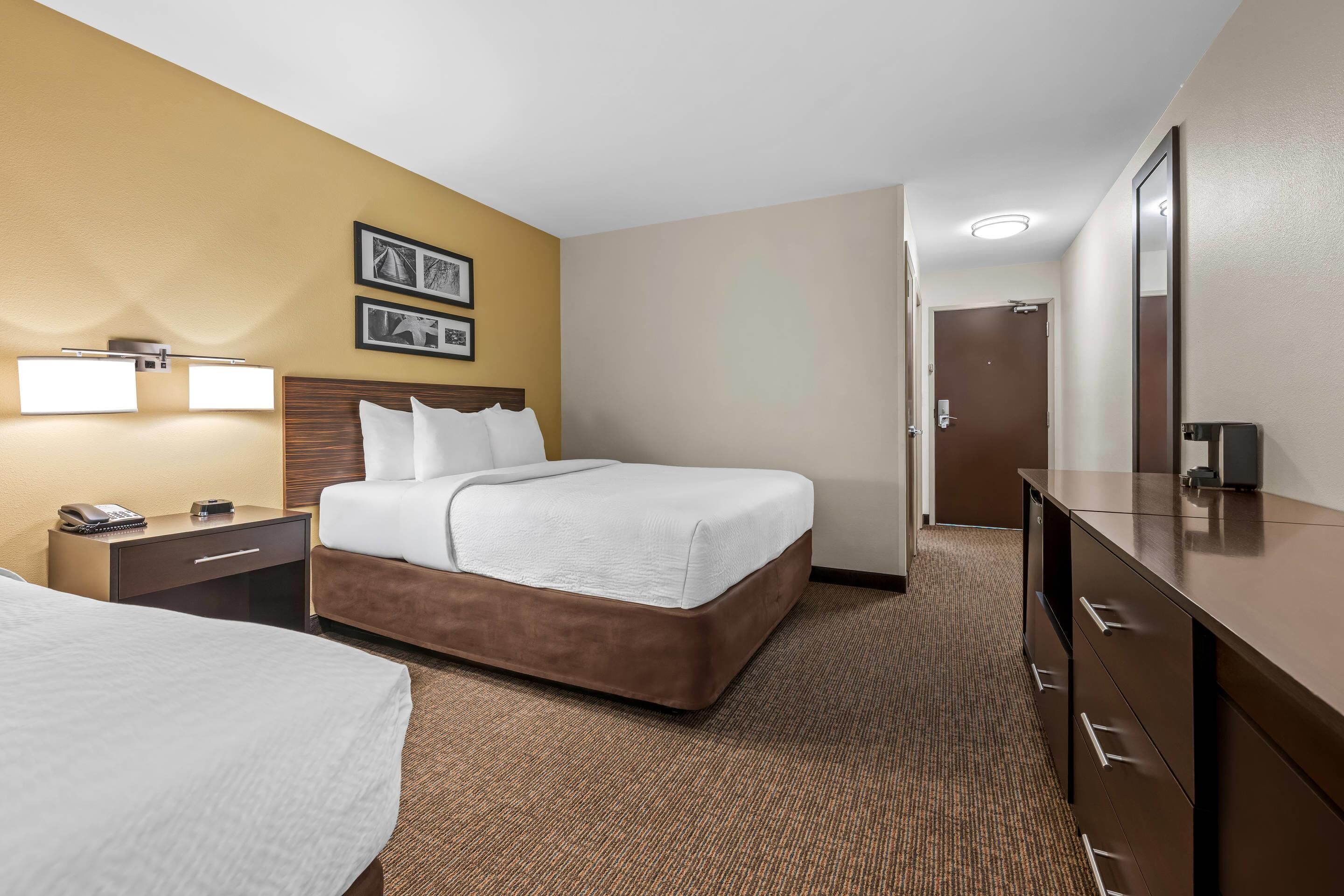 A hotel room with a large bed, bedside tables, a dresser, and a door leading to the bathroom.