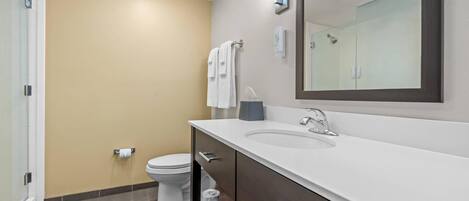 Een moderne badkamer met een behang in beige tint, een wit toilet, een grote spiegel en een witte wastafel met een donkere kast.