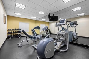 Uma academia com diversos equipamentos de exercícios, incluindo esteiras e aparelhos de musculação, e um suporte com halteres.