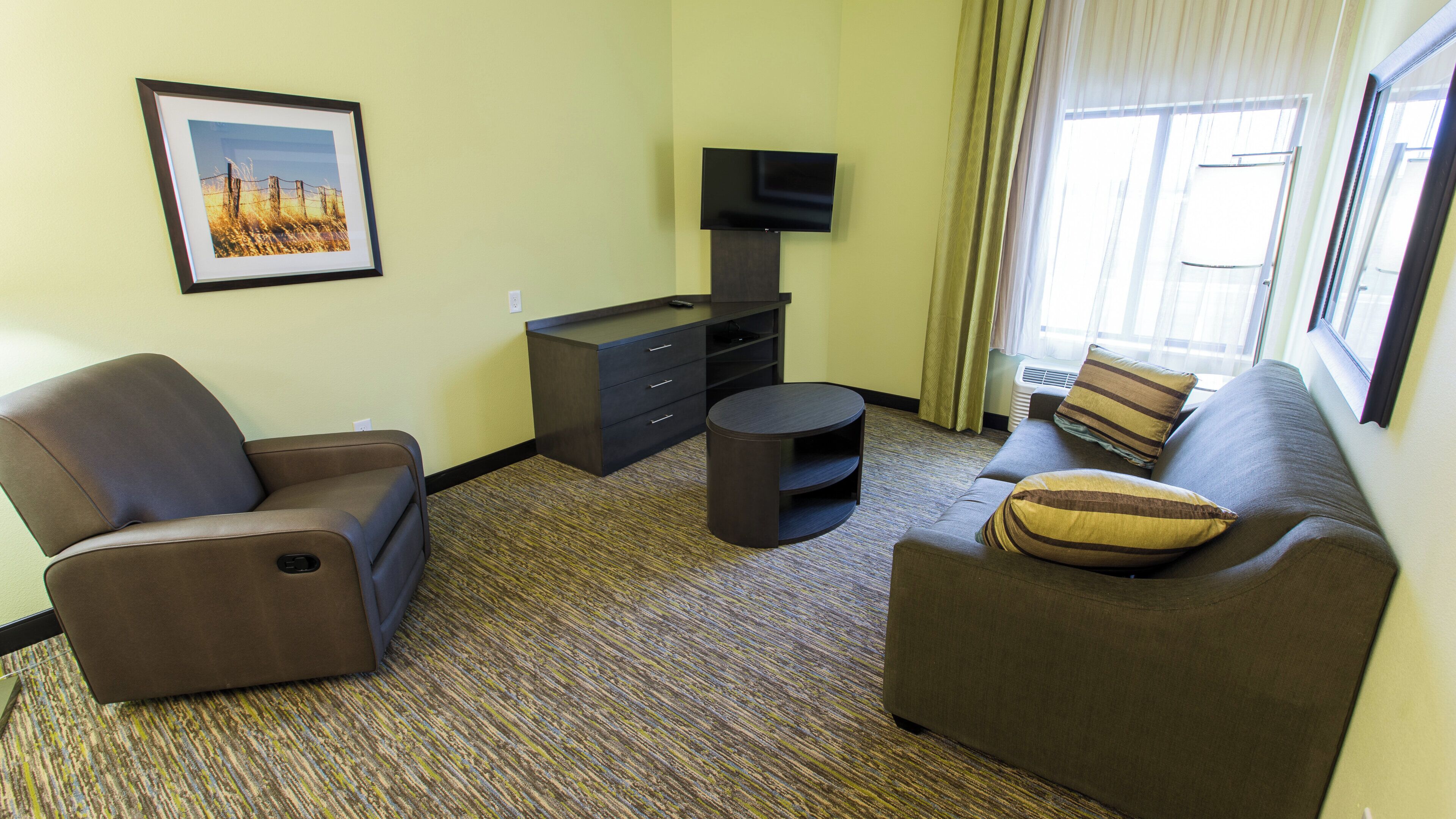 A hotel room with a sofa, armchair, TV, and a framed picture on the wall.