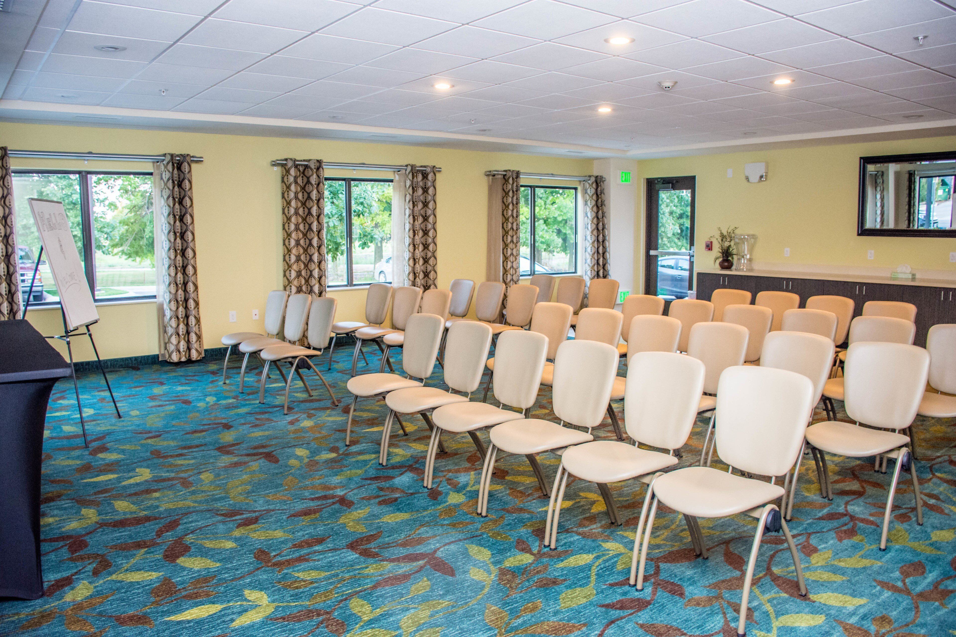 Une salle de conférence avec des rangées de chaises, un pupitre et des fenêtres équipées de rideaux.