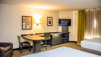 Een hotelkamer met een bed, een bureau met stoel, een televisie en een raam met gordijnen.