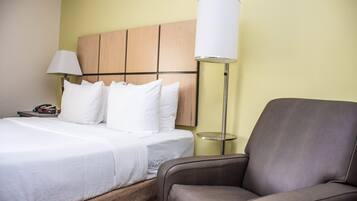 Una habitación de hotel con una cama, una lámpara de noche, una silla y una mesita de noche con un teléfono.