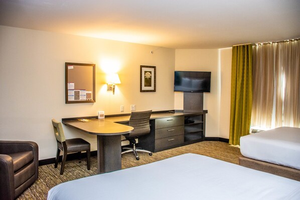 A hotel room with a bed, a desk with a chair, a TV, a mirror, and a window with curtains. - Candlewood Suites : Overland Park - W 135th St by IHG (Overland Park)