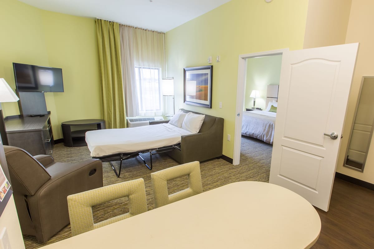 A hotel room with a bed, a desk, a chair, a TV, and a window with curtains.
