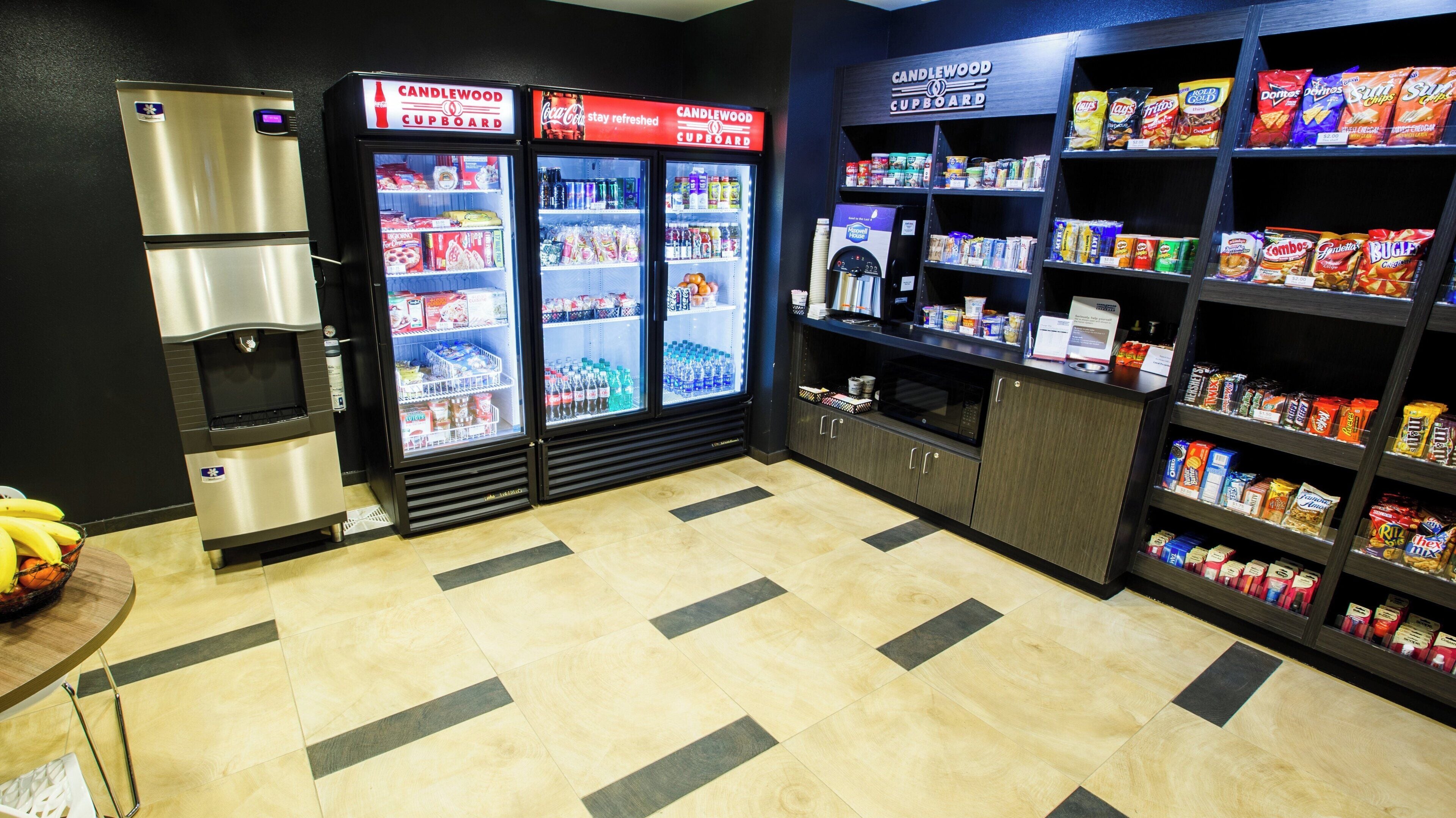 A vending area with a refrigerator, a microwave, and shelves stocked with snacks and beverages.