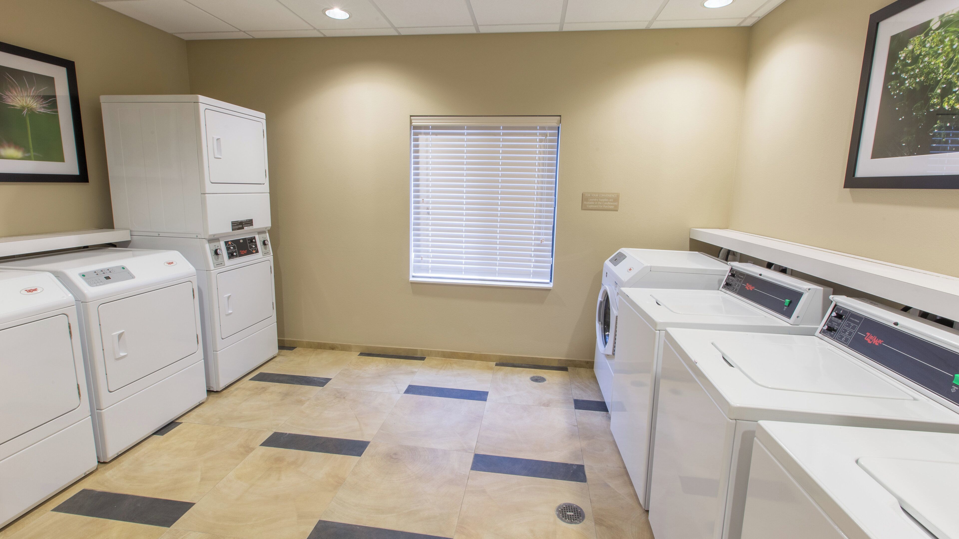 A laundry room with multiple washing machines, a window with blinds, and a tiled floor.